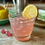 oprah Pink salt recipe lemonade in a glass jar with ice, garnished with a lemon slice.