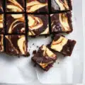 Rich and fudgy cheesecake brownies with a creamy vanilla swirl on top, sliced into squares on parchment paper the perfect chocolate dessert