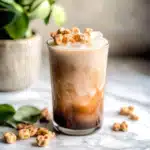 Iced Teddy Graham Latte topped with crushed Teddy Grahams served in a clear glass over ice on a marble countertop