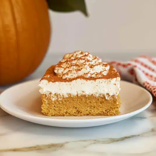 Moist pumpkin tres leches cake topped with whipped cream and cinnamon served on a white plate